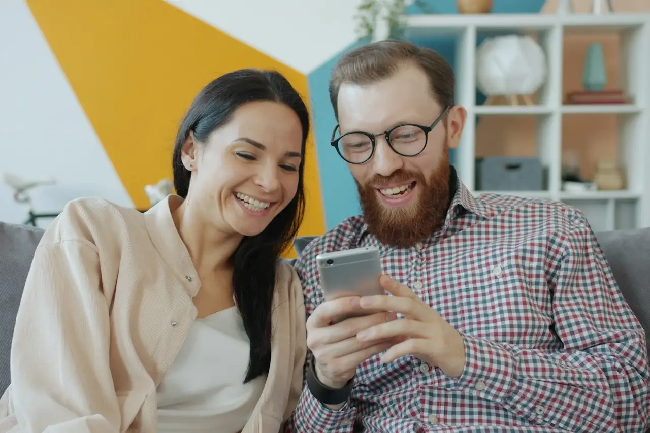 Paar bucht lachend auf dem Sofa per Handy